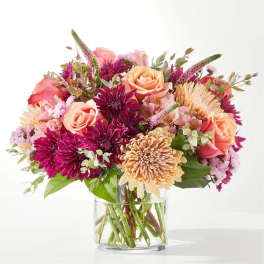 Mixed bouquet of pink, peach, and purple flowers in a clear glass vase
