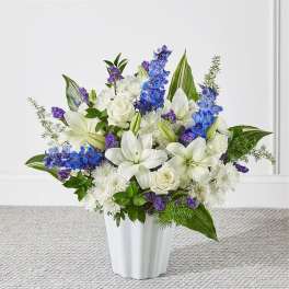 White lilies and roses arranged with blue and purple flowers in a white vase