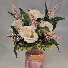 Cream roses and pink filler flowers arranged in a candle jar