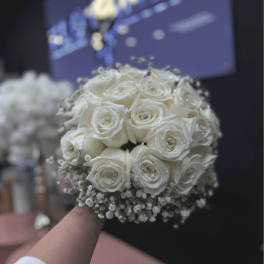 Round bridal bouquet of white roses and baby's breath held in front of a dark background