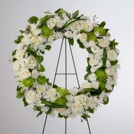 White floral wreath with roses and green accents on a black stand