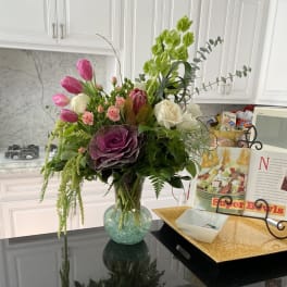 Mixed bouquet of pink tulips, roses, and green orchids in a glass vase