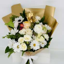 Bouquet of white and cream flowers wrapped in gold paper with a white ribbon