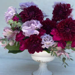 Deep burgundy and lavender flowers arranged in a white pedestal vase