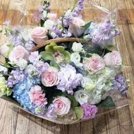 Pastel bouquet of roses, hydrangeas, and lilac flowers wrapped in clear plastic