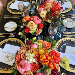 Floral centerpieces on a black-and-gold table setting with glassware and plates