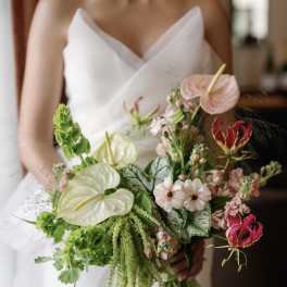 Bride holding a bouquet with anthuriums, orchids, and green trailing flowers