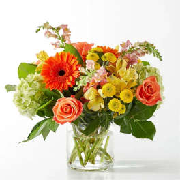 Mixed bouquet of orange roses, gerbera daisies, and yellow blooms in a glass vase