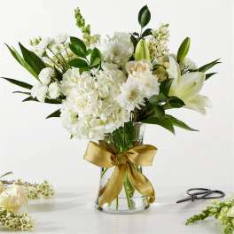 White floral bouquet in a clear glass vase with a gold ribbon