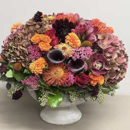 Mixed floral arrangement in a gray pedestal vase with pink, orange, and dark blooms