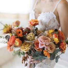 Bride holding a colorful bouquet of roses and orange blooms