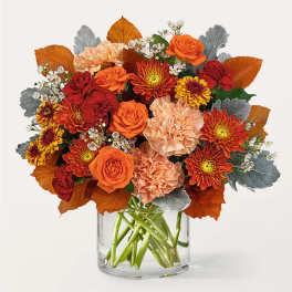 Orange and red bouquet with roses, carnations, and mums in a clear glass vase