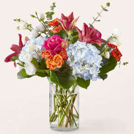 Mixed bouquet of roses, lilies, and hydrangeas in a clear glass vase