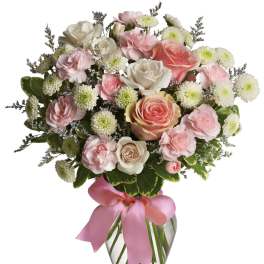 Pink and white bouquet of roses and carnations in a glass vase with a pink ribbon