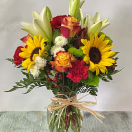 Mixed bouquet of sunflowers, roses, lilies, and carnations in a glass vase