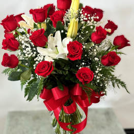 Red roses and white lilies in a clear glass vase with a red ribbon