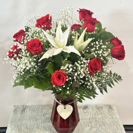 Red roses and white lilies in a red vase with a heart tag