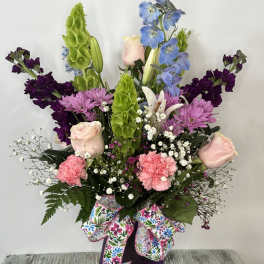 Tall mixed bouquet with pink roses, purple blooms, and blue flowers in a purple vase