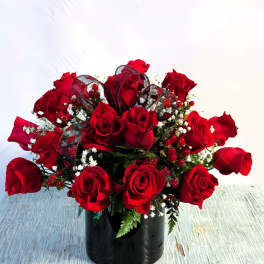 Red roses arranged in a black vase with ribbon and berry accents
