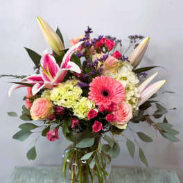 Mixed bouquet in a glass vase with pink lilies, roses, and a gerbera daisy