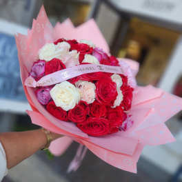 Handheld bouquet of red, white, and pink roses wrapped in pink paper