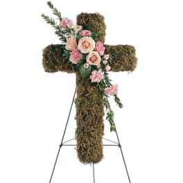 Moss-covered cross with pink roses and carnations on a stand