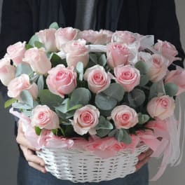 Pink roses arranged in a white basket with ribbon
