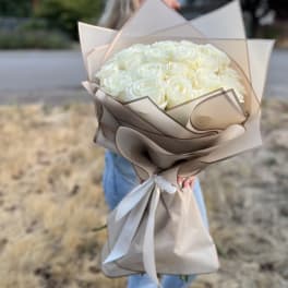 Bouquet of white roses wrapped in beige paper with a white ribbon