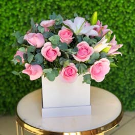 Pink roses and white lilies arranged in a white box