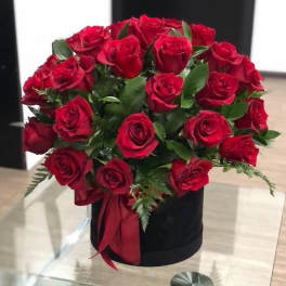 Red roses arranged in a black hatbox with a red ribbon