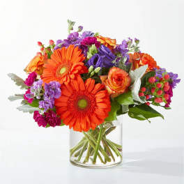 Bright mixed bouquet of orange, purple, and pink flowers in a clear glass vase