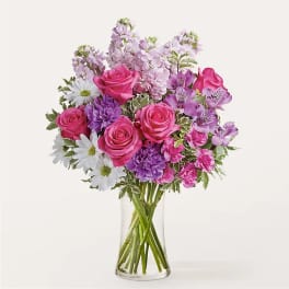 Bouquet of pink roses, purple flowers, and white daisies in a clear glass vase
