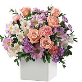 Mixed pink, purple, and white flowers in a white square vase