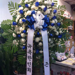 Large standing floral wreath with blue and white flowers and ribbon