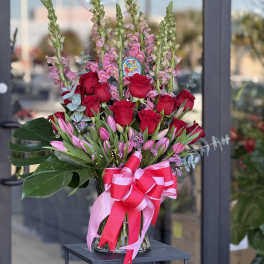 Bouquet of red roses and pink tulips in a glass vase with a pink ribbon