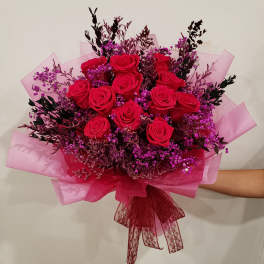 Bouquet of red roses with purple filler flowers wrapped in pink paper