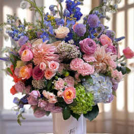 Large pastel bouquet in a white vase with pink, blue, and purple flowers