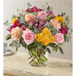 Mixed bouquet of pink, yellow, and peach flowers in a clear glass vase