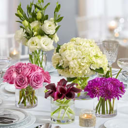 Four floral centerpieces in glass vases on a set table