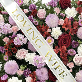 Floral arrangement with roses, chrysanthemums, and alstroemeria under a "LOVING WIFE" ribbon