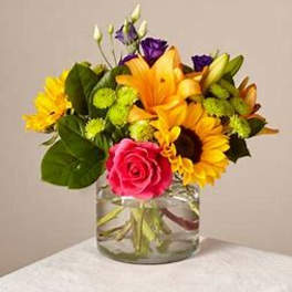 Mixed bouquet with sunflowers, lilies, roses, and purple blooms in a glass vase
