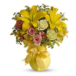 Yellow lilies and roses arranged in a gold vase with a ribbon bow