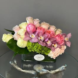 Pink and cream roses with purple orchids in a glass vase