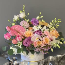 Mixed bouquet with pink tulips, roses, orchids, and anthurium in a white hatbox