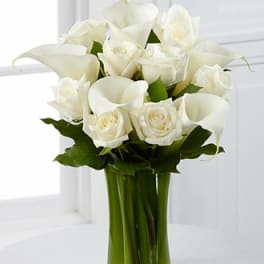 White roses and calla lilies in a clear glass vase