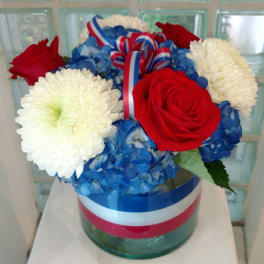 Red roses and white mums arranged with blue hydrangeas in a glass vase.