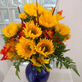 Sunflower arrangement in a blue glass vase with autumn leaves
