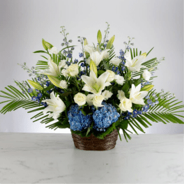 Large white lilies and roses with blue hydrangeas arranged in a basket