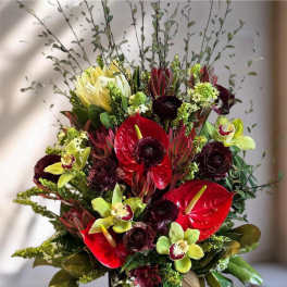 Red anthuriums and green orchids in a black vase