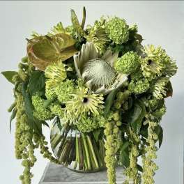 Green floral arrangement in a glass vase with cascading blooms
